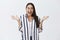 Indoor shot of amazed and thrilled happy woman in eyewear and striped blouse, spreading palms in joy and smiling broadly