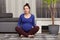 Indoor shot of beautiful European pregnant woman sits in zen posture, keeps legs crossed, has yoga exercises at home, looks