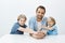 Indoor shot of beautiful happy dad and sons sitting at table and smiling broadly, holding hands and gazing at camera