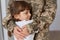 Indoor shot of cute charming girl hugging her mother who comes after war or from army, anonymous woman wearing military uniform