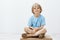 Indoor shot of cute happy blond child with positive smile sitting with crossed hands, having vitiligo, smiling broadly