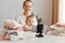 Indoor shot of delighted young adult woman blogger posing with infant daughter in front of tripod with phone, spending time with