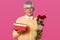 Indoor shot of elderly gentleman with serious facial expression holds gift box and red roses, dressed in yellow shirt with bowtie