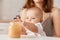Indoor shot of faceless mother feeding her little infant daughter with vegetable puree, charming toddler baby stretching hand to