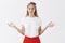 Indoor shot of focused calm and relieved attractive fair-haired woman in red skirt and headband raising hands aside with