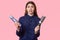 Indoor shot of frustrated European young woman with long dark hair, dressed in dark blue shirt, holds haircomb and hairspray,