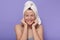 Indoor shot of funny young girl with white towel on her head, lady with coffee scrub on her face, charming woman using cleansing