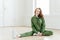 Indoor shot of glad ginger European female wears sports clothes, stretches legs on floor, wears sportshoes, has slim body, has