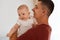 Indoor shot of handsome father wearing burgundy t shirt with charming infant daughter, family expressing happiness and positive