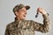 Indoor shot of happy excited soldier man wearing camouflage uniform and cap, showing house keys, mortgage assistance from a