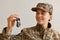 Indoor shot of happy smiling woman soldier wearing camouflage uniform and hat, posing at home, holding and looking at key in hands