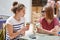 Indoor shot of happy young female friends look joyfully at each other, eat ice cream, discuss something pleasant with cheerful exp