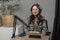 Indoor shot of laughing woman doing podcast. Girl in checkered shirt and headphones using microphone and tablet