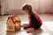 Indoor shot of liitle charming girl sits on floor with her doll house, wearing casual clothing, has ponytail. Self isolation