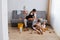 Indoor shot of man washing the floor with a mop at home, sitting on sofa to rest and talk with his daughter who playing on the