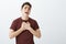 Indoor shot of passionate good-looking boyfriend in trendy red t-shirt, holding palms on heart and singing serenade with