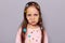 Indoor shot of sad upset little brown haired little girl covered with stickers posing isolated over gray background, feeling bored