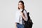 Indoor shot of serious adorable teenager in stylish black hat, carries rucksack, wears white shirt and jeans, isolated over white