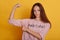 Indoor shot of serious woman with long beautiful hair, wearing pink shirt with inscription, slim female showing her biceps and