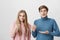 Indoor shot of shocked male and frowning female wearing colourful sweaters looking at camera. Boy pointing with fingers