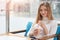 Indoor shot of smiling cute beautiful young female feels relaxed while sitting on comfortable blue sofa in cafe, enjoying fresh