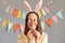 Indoor shot of smiling funny woman wearing rabbit ears hiding her eye with Easter cake pops isolated on gray decorated background