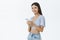 Indoor shot of sociable attractive happy asian female in cropped top holding smartphone wearing wireless earphones and