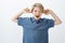 Indoor shot of unhappy annoyed young european child in blue t-shirt, shouting or yelling, covering ears with index