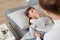 Indoor shot of unhealthy ill female child with handkerchief lying on sofa under blanket suffering runny nose and high temperature