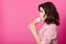 Indoor shot of woman in striped fashionable blouse stands in profile and holds in her hand ice cream on pink studio background,