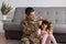 Indoor shot of young adult soldier man wearing camouflage uniform returning home after army, spending time with daughter, wearing