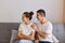 Indoor shot of young couple having conflict, angry offended woman sitting on couch and turning away from husband, having family