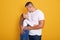 Indoor shot of young handsom man and his daughter hugging and looking at each other, stand smiling isolated over yellow studio