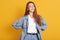 Indoor studio shot of fashionable slender young lady keeping her hands on waist, smiling sincerely, wearing denim jacket, t shirt