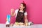 Indoor studio shot of funny singing brunette at kitchen, closing her eyes, opening mouth widely, holding whisk near her face,