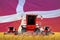 Industrial 3D illustration of four bright red combine harvesters on rye field with flag background, Denmark agriculture concept