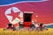 Industrial 3D illustration of four bright red combine harvesters on rye field with flag background, North Korea agriculture