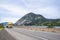 Industrial bright yellow big rig semi truck transporting cargo in dry van semi trailer driving on the divided highway road along