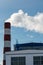 An industrial building and a chimney with white smoke against a blue sky. Air pollution from the smoke of a working factory.