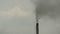 The industrial chimney is emitting exhaust fumes that pollute the environment against dirty and cloudy sky