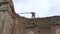 An industrial climber works in protective clothing tied with a safety rope on the emergency roof of a building. Builder