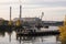 Industrial landscape. Cranes, pipes with smoke. Factory near the river. Pontoon, bridge and barge. Industrial Area