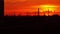 Industrial orange sunset. Sun goes down behind pipes and power pylons. 4K real time long shot