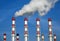 Industrial pipes with white smoke over blue sky. Horizontal photo