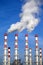 Industrial pipes with white smoke over blue sky. Vertical photo