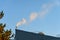 Industrial rooftop with pipe venting steam in early morning light against a blue sky