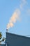 Industrial rooftop with pipe venting steam in early morning light against a blue sky