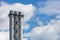 Industrial round smoke-free pipes with an observation deck and a staircase against a clear blue sky with white clouds