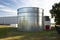 Industrial steel silos standing on the factory grounds on the lawn behind the fence.