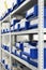 Industrial warehouse. White metal racks with blue plastic trays and cardboard boxes installed in them.